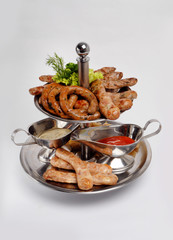 Grilled sausages, greens, red and white sauce on a metal plate on a gray background