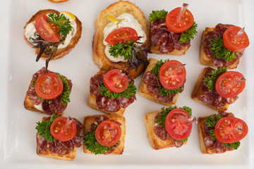 Close-up big plate with serving snack canapes fried bread tomato parsley and salami. Appetizing fresh unhealthy sandwich food decorated on table of luxury restaurant
