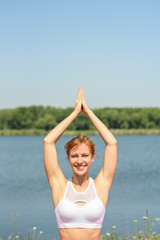 Fototapeta na wymiar Young girl practices yoga near the river on a clear sunny day
