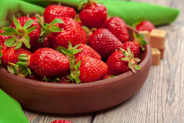 Bowl of strawberry harvest on wooden table close up