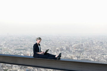Fleißige Frau mit Laptop arbeitet am Laptop auf einem Stahlträger