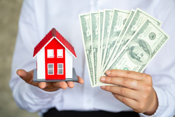 Business man's hand, red roof house, placed on the right hand And hold the left banknote Real estate concepts, home buying, home owners, renting, loans, mortgage buying a home for the future.