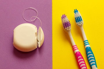 Two toothbrushes and dental floss . Yellow and violet background