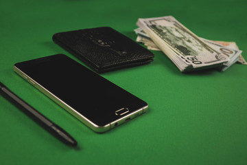 a lot of cash packs, telephone, black pen and wallet lying on a green background