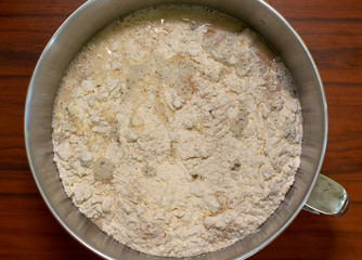 Ingredients of bread dough in a metal mixing bowl, top view