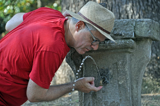 Mann mit Strohhut trinkt aus alter Trinkwasserfontäne