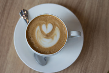 A cup of hot latte art coffee on wooden table background
