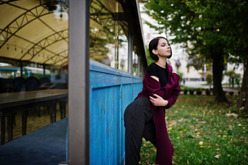 Fototapeta premium A tall leggy young beautiful and elegant model woman at claret coat.