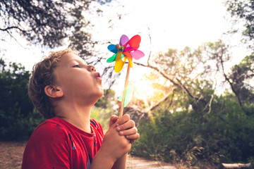 Little handsome boy blows a pinwheel in a forest, carefree, with faded tones and retro style.