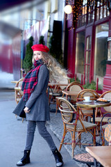 girl with a street in a gray coat with long curls is spinning near a cafe
