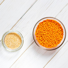 Glass plates with red lentils, sesame seeds and a large glass plate stand on wooden table
