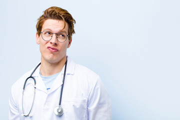 young red head doctor looking puzzled and confused, wondering or trying to solve a problem or...