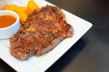Grilled beef steaks served with fresh salad, hash browns potato and spicy sauce on white dish....