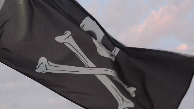 Black Pirate Flag waving in the wind. The Jolly Roger Flag Pirates Flag flying on a flagpole. The black and white flag with skull and crossbones flying from mast of sailing boat. Ragged pirate. Sea
