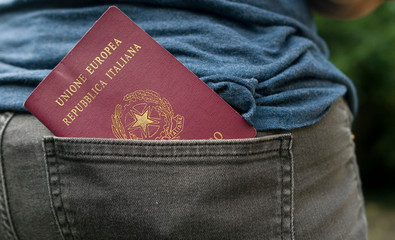 Adult woman holding her Italian passport in the back pocket of trousers, red, identity document used to cross borders and travel the world, ready to go, Milan, Italy