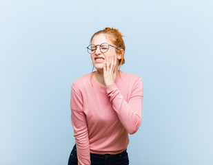 young red head pretty woman holding cheek and suffering painful toothache, feeling ill, miserable...