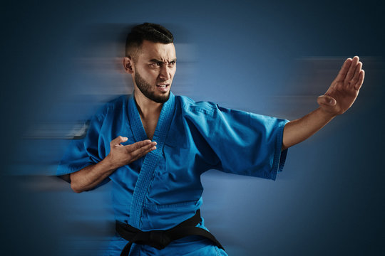 Asian Kazakh karate fighter in kimono uniform is combat on blue background with copy space isolated