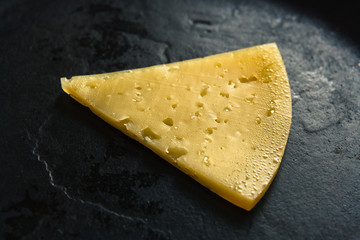 A piece of yellow porous cheese on a black cast-iron background.