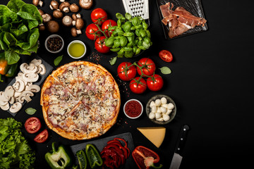 Homemade pizza ready to eat with raw ingredients. Top view on a black background.