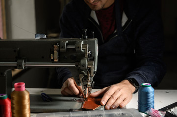 Working process of leather craftsman. Tanner or skinner sews leather on a special sewing machine, close up.