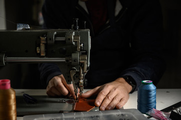 Working process of leather craftsman. Tanner or skinner sews leather on a special sewing machine, close up.