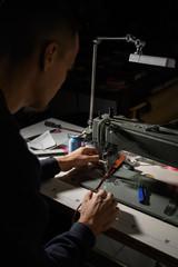 Working process of leather craftsman. Tanner or skinner sews leather on a special sewing machine, close up.