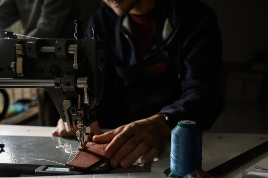 Working process of leather craftsman. Tanner or skinner sews leather on a special sewing machine, close up.