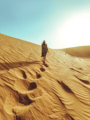 Young beautiful woman in a long dress walks along the sand dunes of the Dubai desert