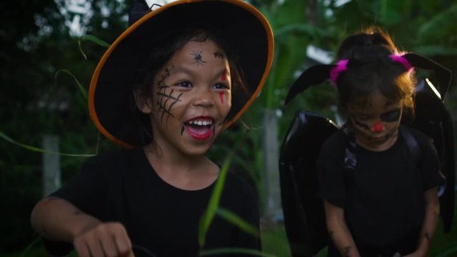 Asian little girls with a painted face is walking in the dark woods to celebrating in halloween. The children in demon costumes is spell enchant so enjoyment in halloween. Kids trick or treat.