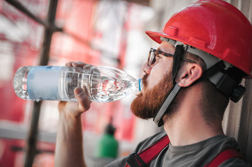 Construction mason worker on scaffolding, resting and drinking water