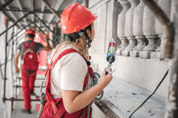 Female construction mason on the scaffolding, working with silicone gun