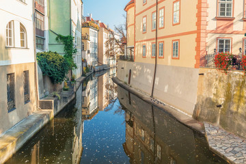 Fototapeta na wymiar River between old houses with flowers with reflection in autumn