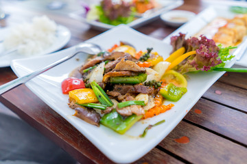 The selective focus of roasted duck meat decorated with colorful fried vegetables and pepper placed on the wooden table with jasmine rice in restaurant