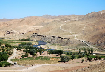The Hari River (Harirud) near Chisht-e-Sharif in  Herat Province, Afghanistan. The river flows past a small village in this remote part of western Afghanistan. Trucks are on the dirt road to Herat.