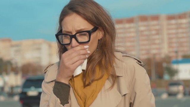 Sad young woman with glasses walk coughs feel sick sneeze holds a handkerchief at outdoor fever cold allergy female nose sneeze lady runny tissue air pollution adult illness district slow motion