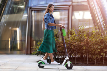 Carefree young woman riding an electric scooter - obrazy, fototapety, plakaty