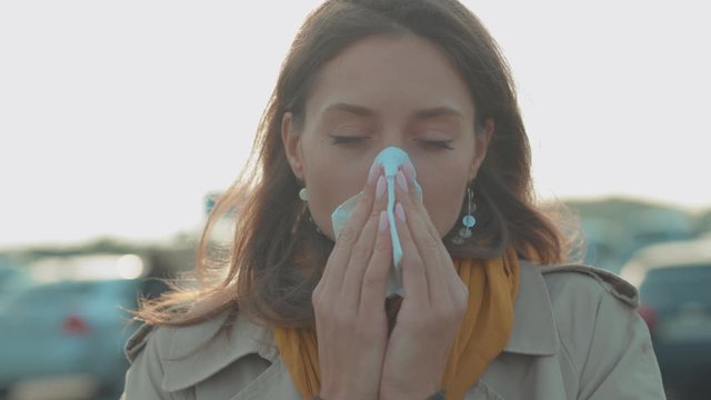 Face young woman stand coughs feel sick sneeze holds a handkerchief at outdoor fever cold allergy female nose sneeze lady runny tissue air pollution adult illness district slow motion
