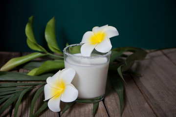Obraz na płótnie Canvas Glass of coconut milk with flowers plumeria and palm leaf on the wooden background
