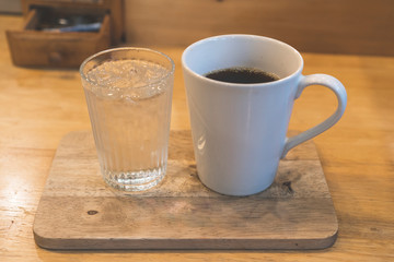 A white coffee mug and a cold glass placed on a wooden plate in a coffee shop