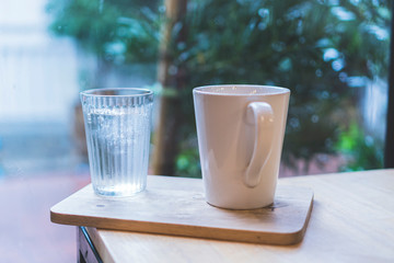 A white coffee mug and a cold glass placed on a wooden plate in a coffee shop