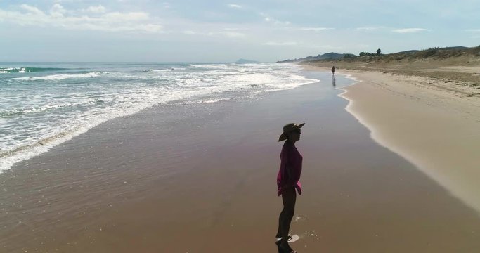 Mujer feliz pasea y da vueltas en playa de arena dorada y un dron la sigue