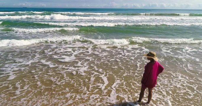 Mujer con pamela mira pensativa el horizonte del mar y un dron vuela