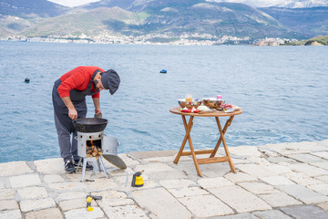 Caucasian man makes a fire under a cauldron for a pilaf with a gas burner
