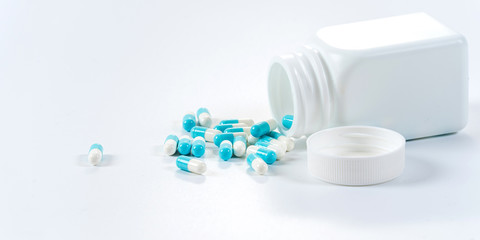 Fototapeta na wymiar Blue and white capsules pills pouring from the bottle on white background