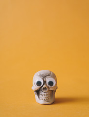 Halloween skeleton head with  googly eyes and orange background. Funny holiday flat lay concept.