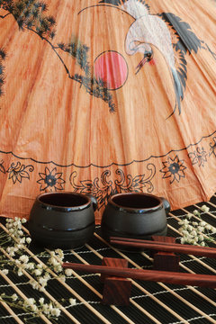 View of two black cups for sake, wooden chopsticks for sushi on a background of a beige picture with storks and the sun