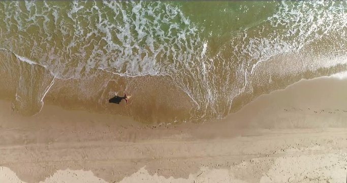 Vista cenital dron de mujer con sombreo paseando en arena dorada y olas blancas