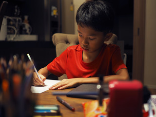 Closeup of Asian boy doing his homework at night. Selected focus.