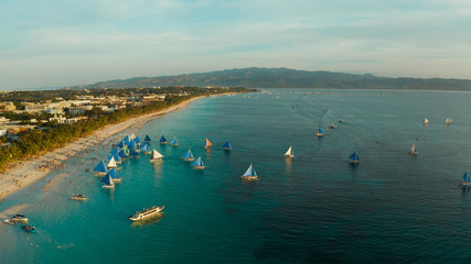 Fototapeta na wymiar Aerial view of sailing boats on the sandy beach of Boracay Island at sunset time. Tropical white beach with sailing boat. Summer and travel vacation concept.
