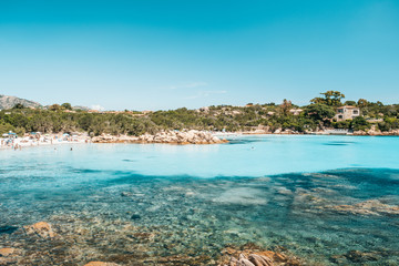 Beach with people enjoying in the crystal clear waters of Sardinia, Italy 